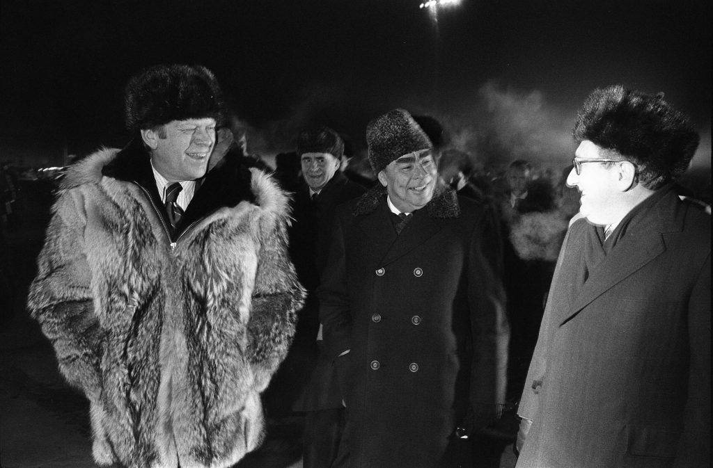 Photograph of President Gerald Ford, General Secretary Lenoid Brezhnev, and Henry Kissinger speaking informally at the conclusion of the Vladivostok Summit on the tarmac at Vozdvizhenka  Airport. Just moments after this photo was taken, President Ford informally concluded the Vladivostok Summit by giving his wolfskin coat to Secretary Brezhnev.